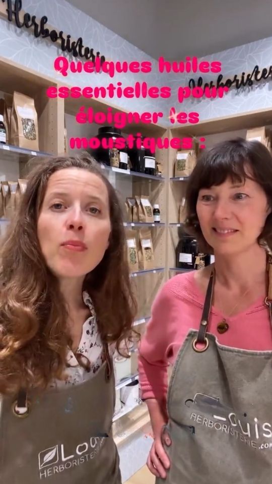 Deux herboristes en tablier dans leur boutique présentant des huiles essentielles pour éloigner les moustiques.