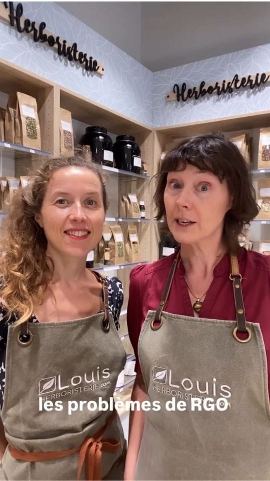 Deux femmes portant un tablier Louis Herboristerie devant des étagères remplies de sachets de plantes et de tisanes, avec le texte incrusté les problèmes de RGO.